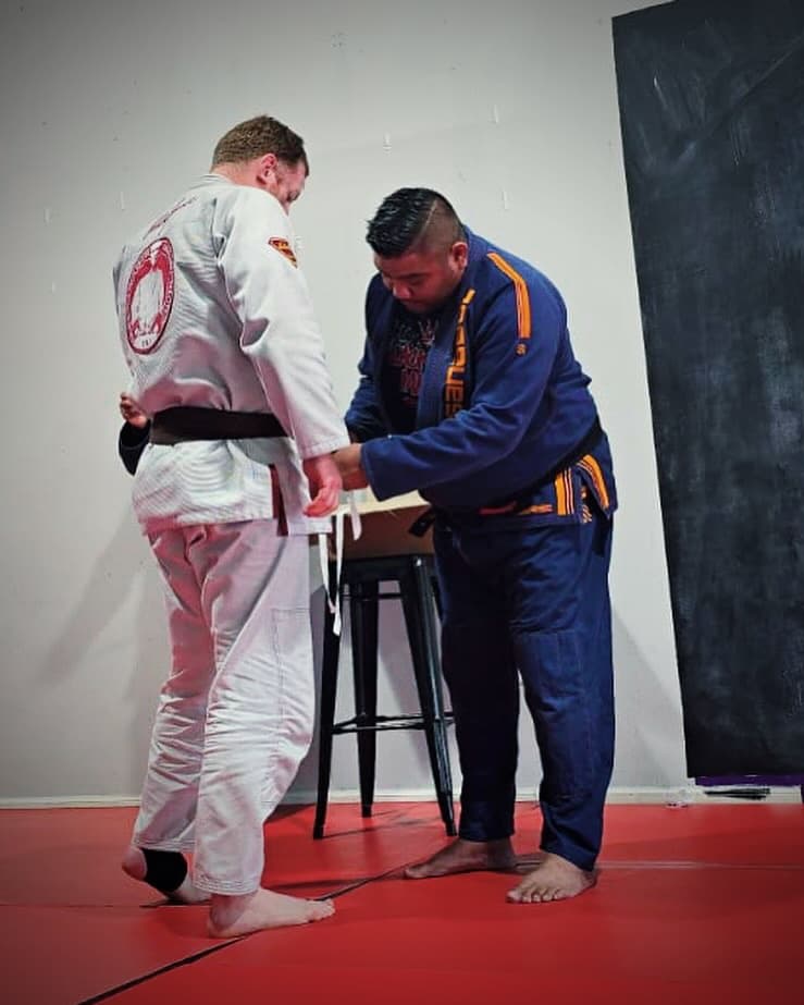 A professor ties a newly earned belt around a student's waist