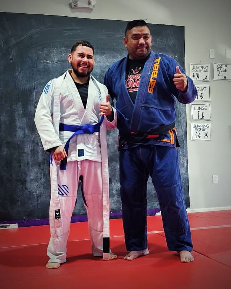 Two Brazilian Jiu-Jitsu students in white and blue gis after a belt promotion