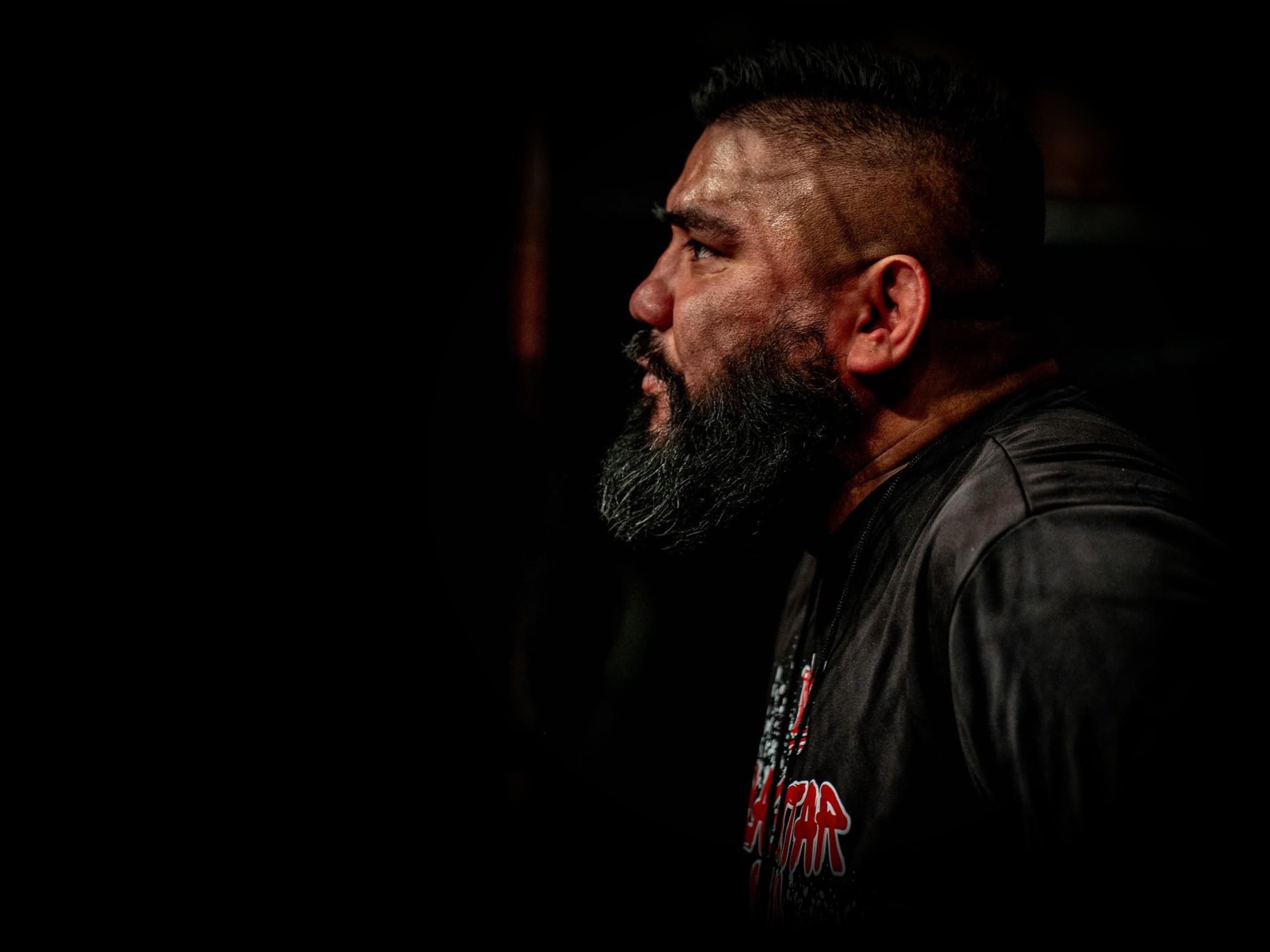 A coach stands in the dark gym, lit by a single overhead light