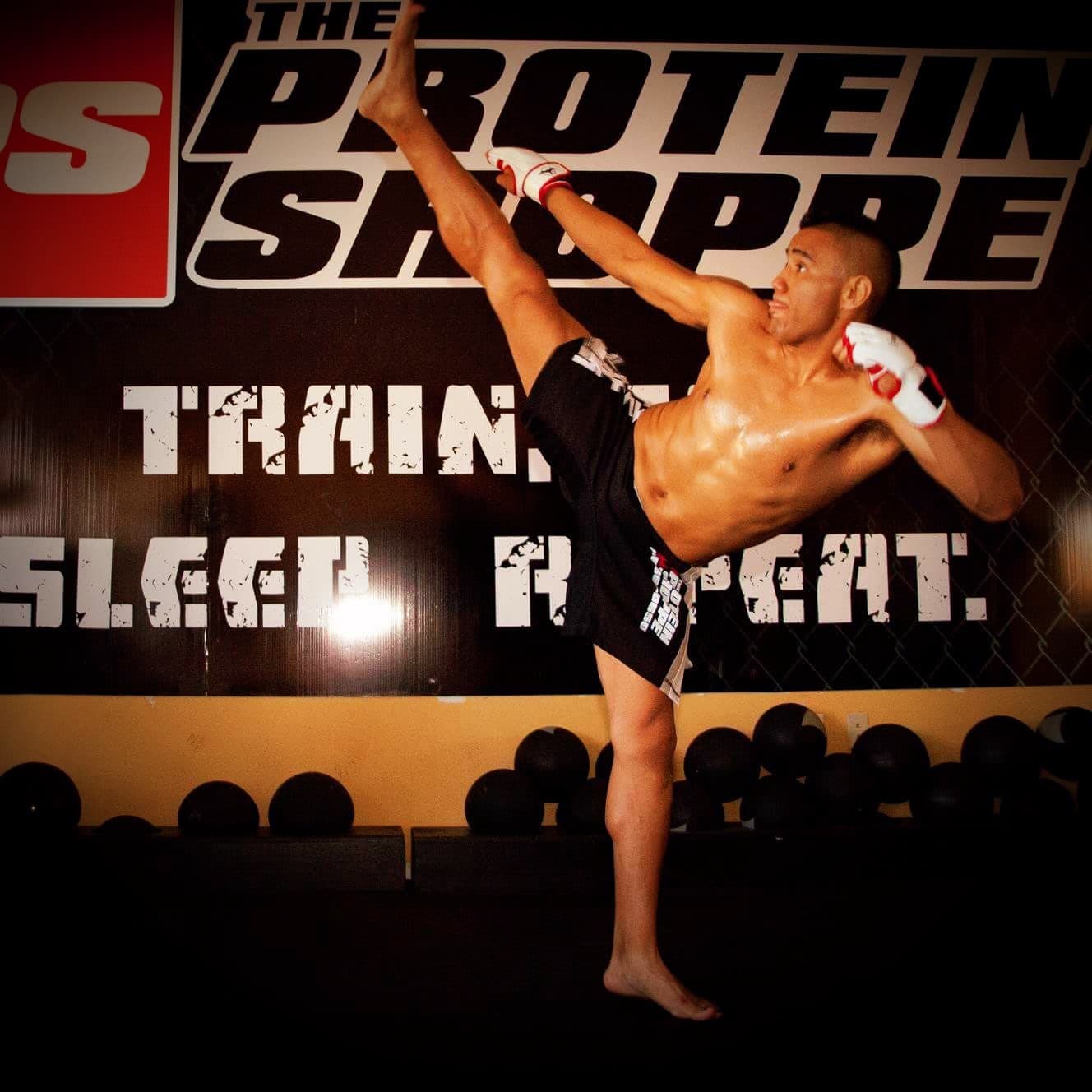 A fighter throws a high kick in front of the Train Sleep Repeat mural at the gym