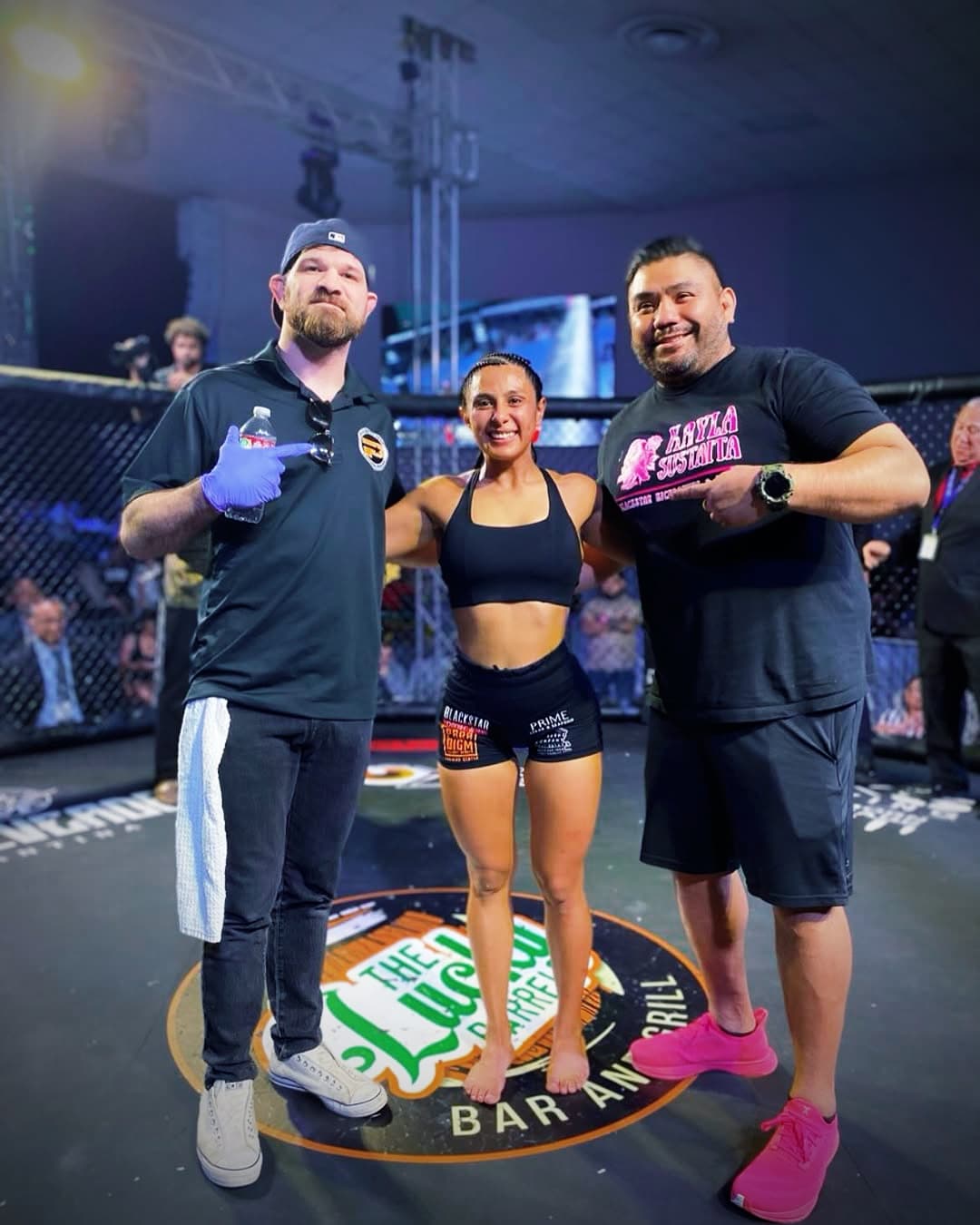 A fighter celebrates with her corner team inside the cage after a bout