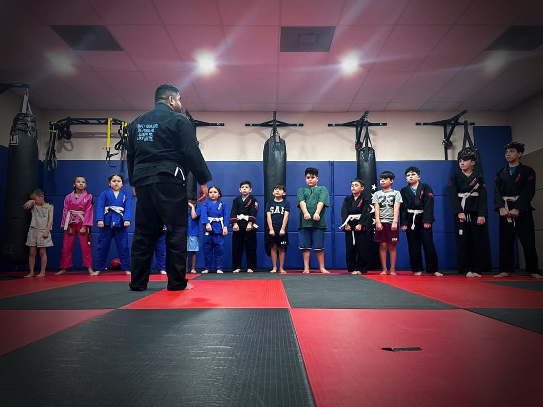 A coach walks the line of young students on the mats under a single light