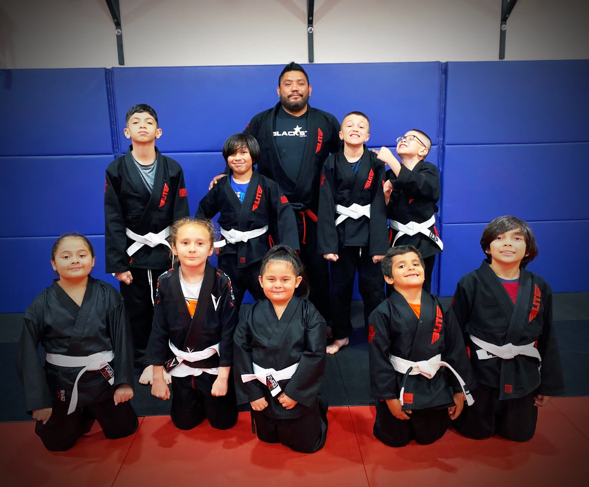 Youth students in black gis line up with their coach on the blue mats